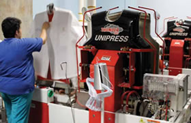 An employee processes a chef coat on a shirt press in dry-cleaning.